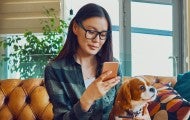 Woman sitting on couch with dog using her phone 