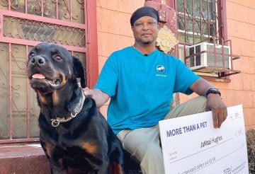 Jamal Hughes holding a large check, sitting next to a dog