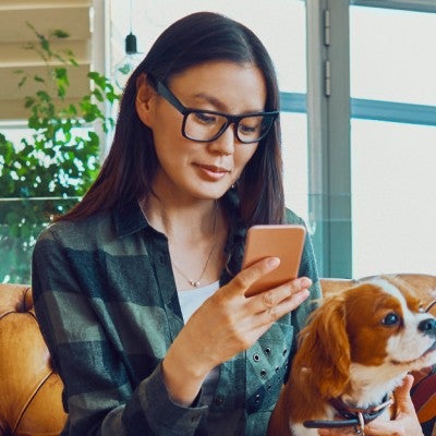 Woman sitting on couch with dog using her phone 